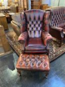 A Chesterfield oxblood high back wing armchair and foot stool