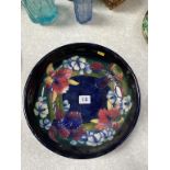 A Moorcroft shallow circular bowl, on dark blue ground, decorated with flowers, 27cm diameter