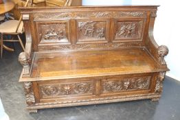 An early 20th century heavily carved oak settle, with carved panelled back and rising seat