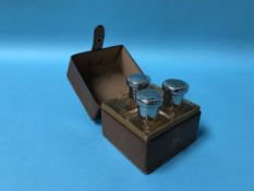 A small brown leather travelling vanity box, containing three plain glass scent bottles