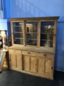 A large pine farmhouse kitchen dresser, the top with three sliding glass doors, below three short