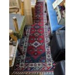 A hand woven Turkish red ground runner having geometric designs and fringed ends, 317 cm x 82 cm