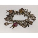 A silver charm bracelet with mixed charms to include a heart shaped locket, four leaf clover, teapot