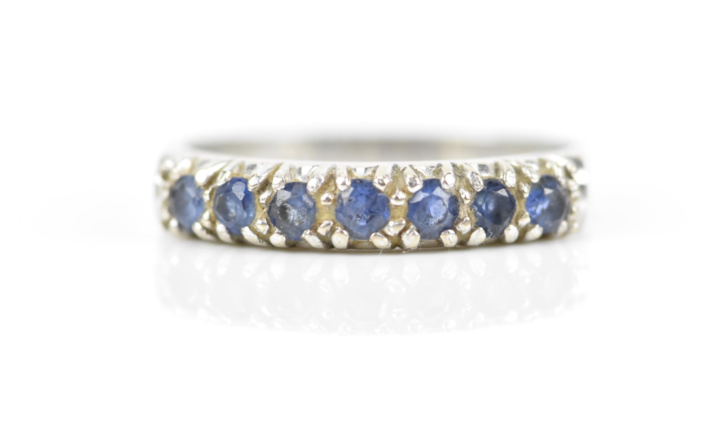 A 9ct white gold and blue sapphire half eternity ring, set with a row of seven same-sized pave-set