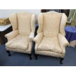 A pair of early 20th century beige upholstered wing back armchairs standing on ball and claw feet