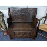 An early 20th century oak carved monk's bench having floral and scroll carving and a hinged seat