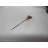 A yellow metal stick pin fashioned as a hand holding a faux pearl Location: