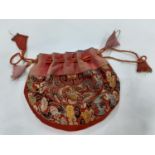 A small Chinese red machine embroidered drawstring pouch with images of dragons and clouds on a