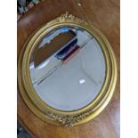An early 20th century oval gilt framed wall mirror with flower and leaf decoration, beaded edge rim,