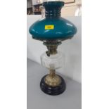 A Victorian oil lamp having a clear glass reservoir and a green shade on a brass stand and black