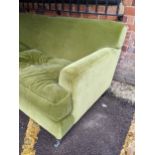 An upholstered three-seater sofa in plush green velvet fabric with matching loose seat cushions,