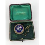 An early 20th century 9ct gold and enamel on copper brooch, decorated with roses on a blue ground,