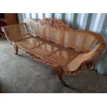 A 19th century colonial hardwood sofa having a floral carved frame, scrolled arms, cane upholstery