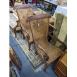 A pair of 19th/20th century Colonial hardwood armchairs having scroll shaped arms, cane seats and