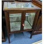 An early 20th century mahogany display table having twin bevelled glass doors and on squared legs,