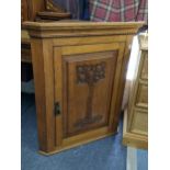 An Art Nouveau oak wall hanging corner cabinet having a dental moulded cornice and single carved