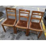 A set of three early 20th century oak ladder back dining chairs on octagonal carved legs and H-