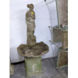 A weathered concrete stone garden fountain in the form of a classically dressed maiden with a vase