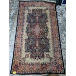 A small Persian handwoven rug with floral design on a blue ground, triple guard border and tasselled