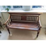 A Thai stained softwood bench with a carved and spindle back and slatted seat on turned legs,