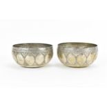 A pair of possibly Indian white metal bowls, designed with embossed work to the body, the