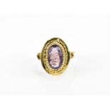 A yellow metal and amethyst dress ring, the oval cut stone in rub-over setting with ropetwist detail