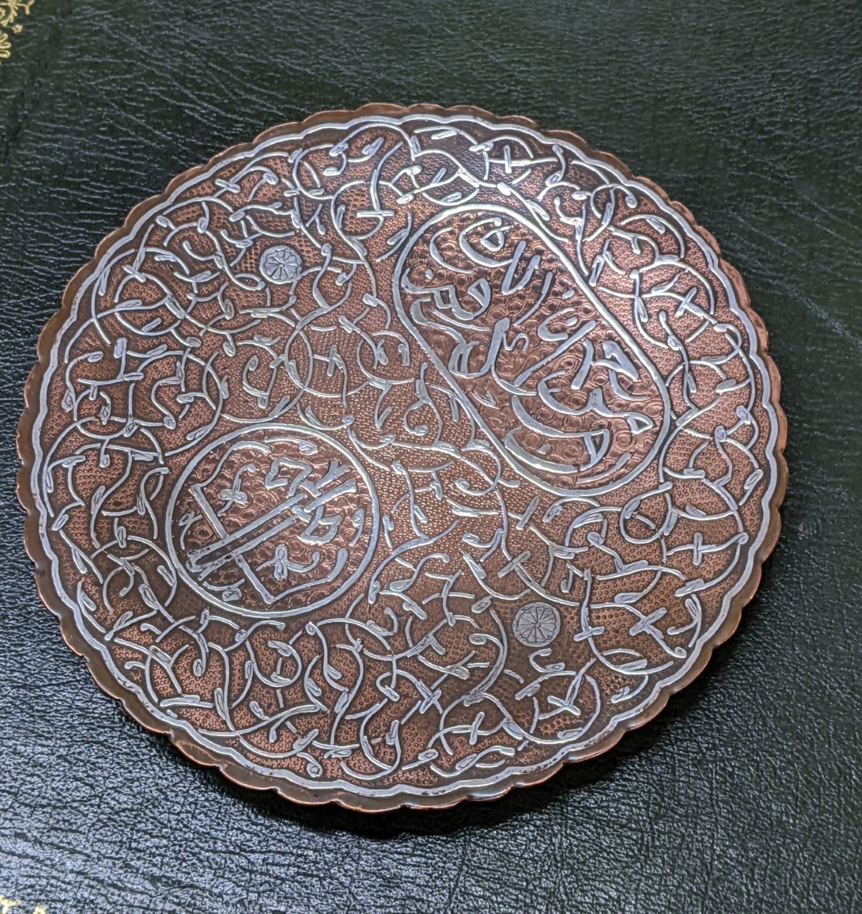 An Islamic, Cairo, inlaid silver on copper dish, with panels of text and scrolls, on three ball