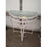 A vintage white painted metal demi lune table having a glass top and scrolled supports Location: