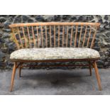 A mid century elm and beechwood Ercol loveseat, with cushion, spindle back, raised on tapered turned