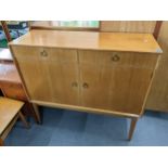 A retro Gordon Russell teak cabinet having two drawers above two cupboard doors and on tapering legs