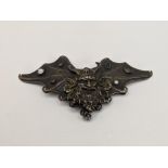 A white metal belt buckle with embossed decoration of a mask and wings with one inset stone, 58.5g