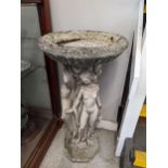 A weathered garden concrete bird bath, the circular bowl held on a column depicting the Three
