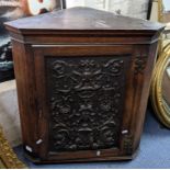 An early 20th century oak wall hanging corner cabinet having a heavily carved door, 68cm h x 61cm