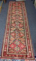 A Kurdish hand woven runner having seven diamond motifs on a red ground, 327 x 96, Location: