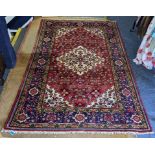 A Persian hand woven rug having a floral design on a red ground with tasselled ends, 218.5cm x 149cm