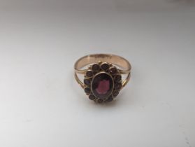 A vintage yellow metal garnet cluster ring, inset with central garnet surrounded by twelve
