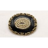 A 19th century mourning black enamel mourning brooch, set with seed pearl and a scroll work frame