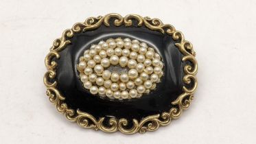 A 19th century mourning black enamel mourning brooch, set with seed pearl and a scroll work frame