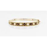 A 9ct yellow gold, pearl and garnet set bangle, set with graduated alternating pearl and red