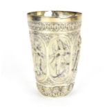 A Colonial Indian white metal goblet, of tapered form with deep embossed deities in oval panels,