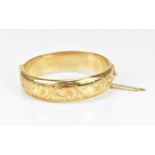 A 9ct yellow gold bangle, with engraved foliage to the exterior, the clasp with safety chain, 6 cm