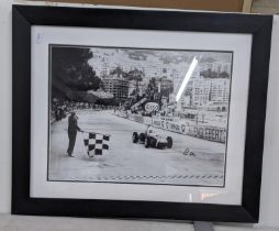 A black and white reprinted photograph of Stirling Moss in a car, signed Location: