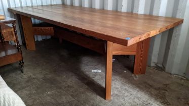 A large refectory pitch pine dining table having four block shaped legs united by a single,