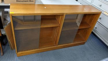 A retro teak bookcase having glazed sliding doors and on a plinth base, 77cm h x 136cm w Location: