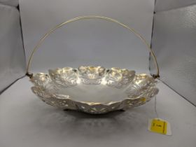A white metal sweet dish elaborately decorated with pierced emblems with a swing handle, the base