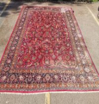 A handwoven Persian Mashad rug, with large central rectangular red ground decorated with shah