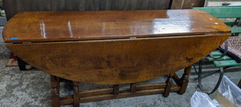 A large oak gateleg coffin style dining table, oval top on turned skim baluster legs, united by