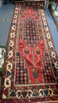 An Iranian hand woven runner having a red ground with a central motif, repeating patterns and