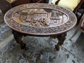 An Anglo-Indian carved wood coffee table, oval top carved in relief with four figures pulling an
