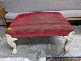 A large footstool upholstered in a red checkered pattern, on white painted legs in the form of an